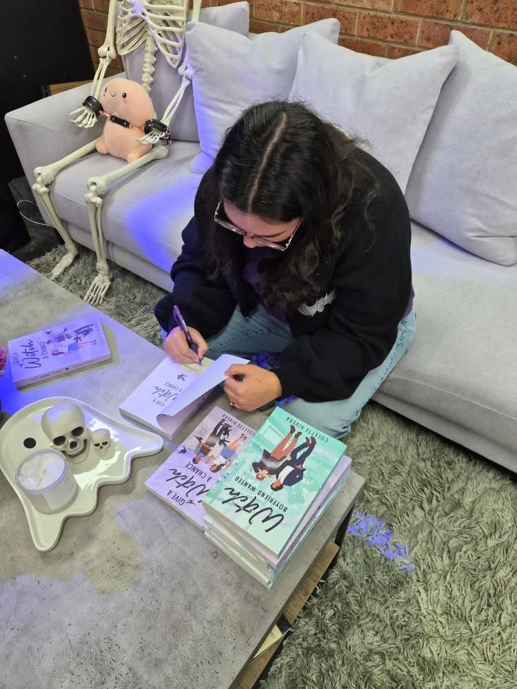 a photo of Colette signing books (face obscured, looking down) at A thousand Lives Bookshop